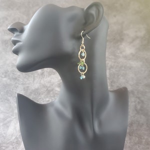 May include: Gold dangle earrings with blue and green crystal beads and three gold hoops.