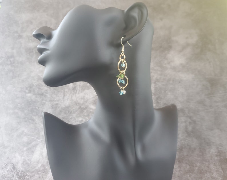 May include: Gold dangle earrings with blue and green crystal beads and three gold hoops.