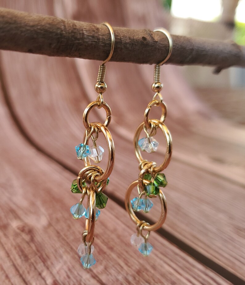 May include: Gold dangle earrings with multiple linked circles and blue, green, and clear crystal beads.