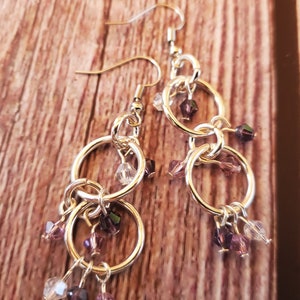 May include: Silver dangle earrings with multiple linked circles and dangling purple and clear crystal beads.