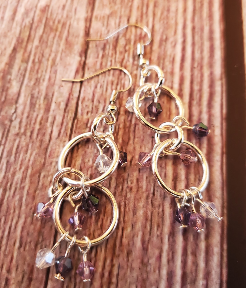 May include: Silver dangle earrings with multiple linked circles and dangling purple and clear crystal beads.