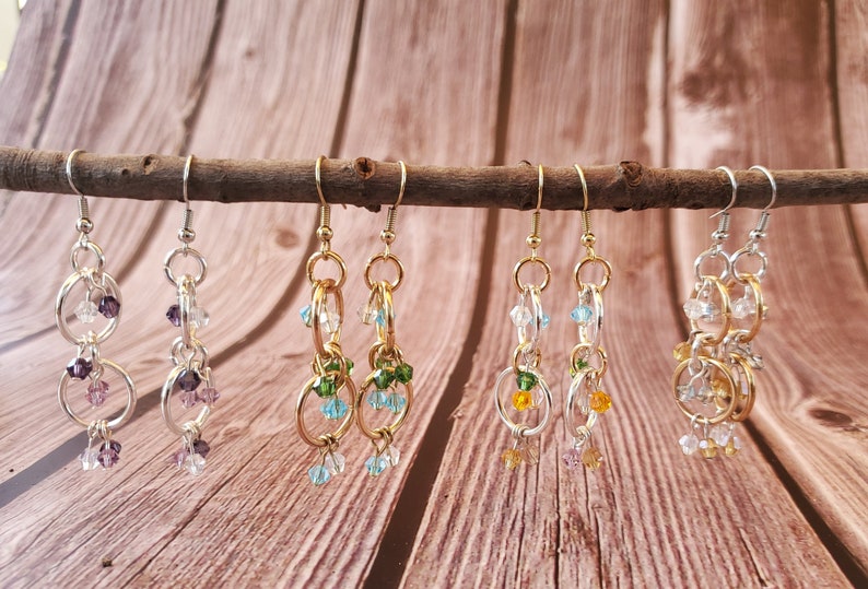 May include: Six pairs of dangle earrings with multiple gold and silver rings and crystal beads in various colors, including purple, green, blue, and orange.