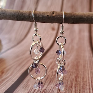 May include: Silver dangle earrings with multiple linked circles and dangling crystal beads in shades of purple and clear.