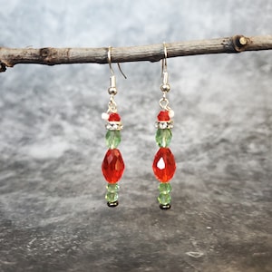 May include: A pair of dangle earrings with red and green crystal beads. The earrings have a silver tone and are accented with rhinestones.