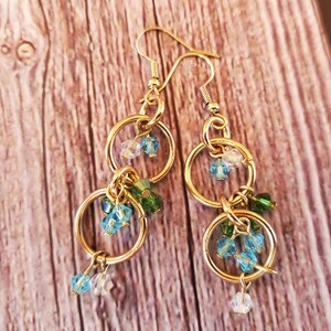 May include: Gold dangle earrings with multiple small blue and green glass beads hanging from two gold hoops.