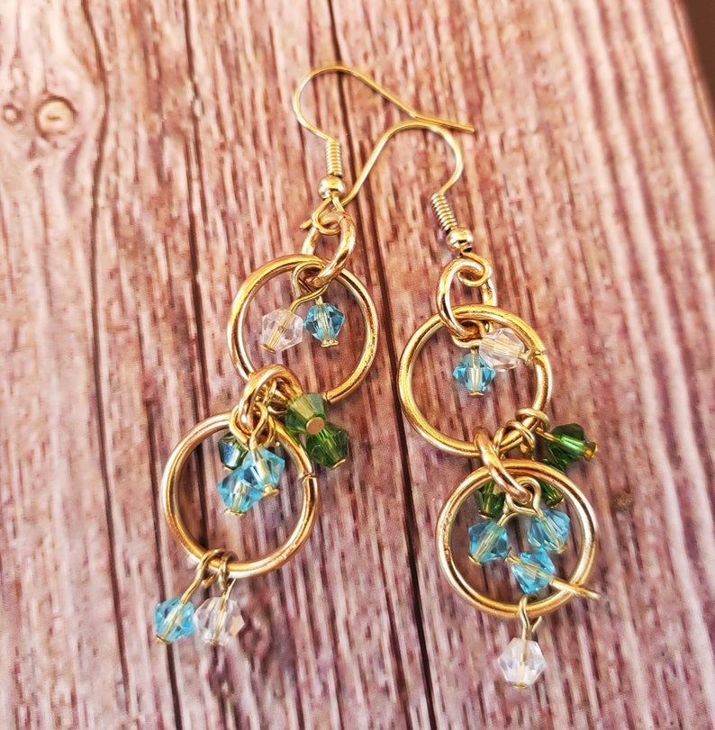 May include: Gold dangle earrings with multiple small blue and green glass beads hanging from two gold hoops.