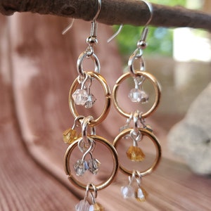 May include: Gold and silver dangle earrings with multiple crystal beads. The earrings feature two interlocking circles with a dangling crystal bead.