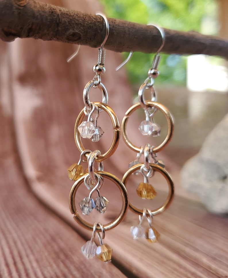May include: Gold and silver dangle earrings with multiple crystal beads. The earrings feature two interlocking circles with a dangling crystal bead.