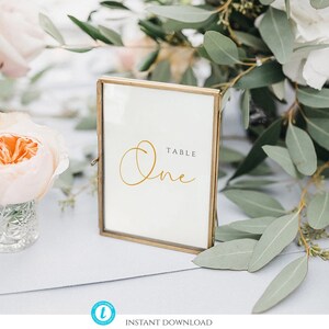 May include: A gold-framed table number sign with the word "Table" and the number "One" written in a cursive font.