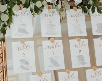 May include: A gold framed seating chart with 14 table cards. Each card is labeled with a table number and guest names. The frame is ornate, and the chart is decorated with white flowers and greenery. The text "INSTANT DOWNLOAD" is at the bottom.