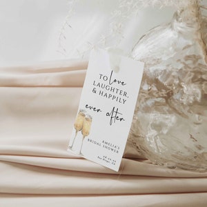 Pu&ograve; includere: Un biglietto bianco con testo nero che recita "To love laughter & happily ever after" con un'illustrazione ad acquerello di due flute di champagne. Il biglietto include anche il testo "Amelia's Bridal Shower 08.22.22 San Diego, CA."