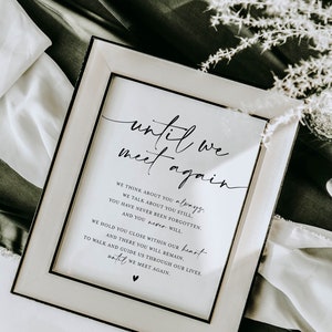 May include: A framed print with the words "until we meet again" in elegant script. The print includes a heartfelt message about remembrance and love. The frame is a light cream color with a textured design, set against a dark green and white fabric.
