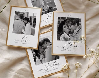May include: Four gold-framed table number cards with black and white photos of a couple. The cards have the text "Table One", "Table Eleven", "Table Sixteen", and "Table Two".