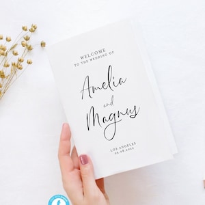 May include: A white wedding program with the text "Welcome to the wedding of Amelia and Magnus" in black calligraphy. The date and location of the wedding are also included: "Los Angeles 09.08.2022".