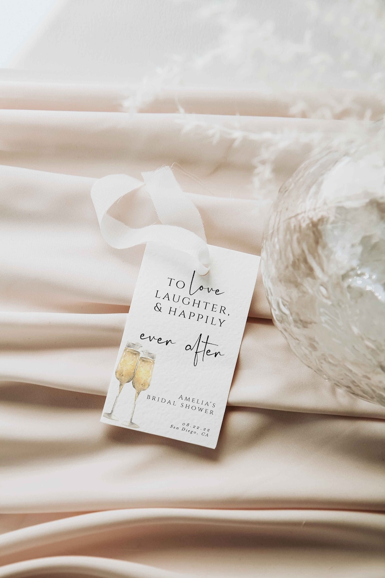 Pu&ograve; includere: Un'etichetta bianca con testo nero che recita "To love laughter, & happily ever after" con un'illustrazione ad acquerello di due flute di champagne. L'etichetta include anche il testo "Amelia's Bridal Shower 08.22.22 San Diego, CA."