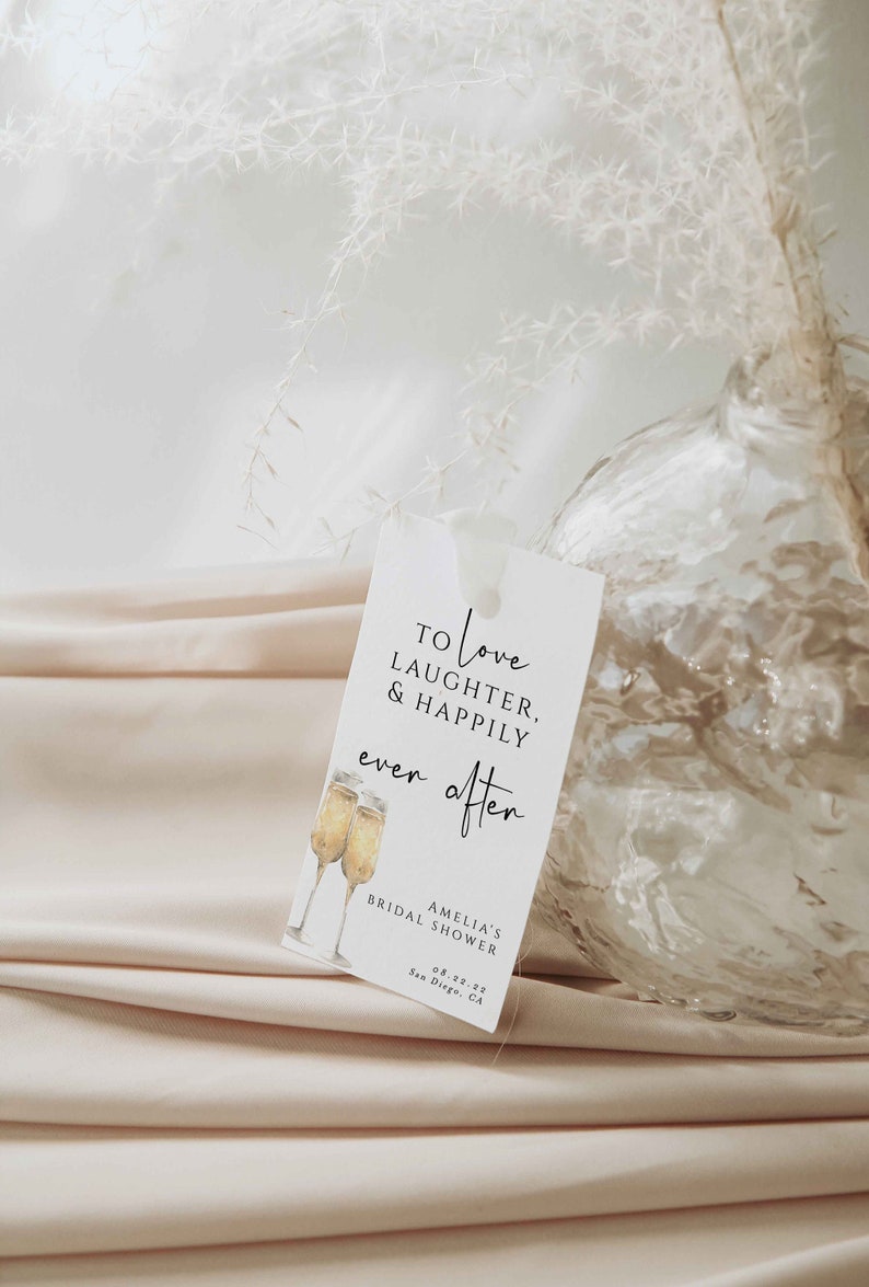 Pu&ograve; includere: Un biglietto bianco con testo nero che recita "To love laughter & happily ever after" con un'illustrazione ad acquerello di due flute di champagne. Il biglietto include anche il testo "Amelia's Bridal Shower 08.22.22 San Diego, CA."