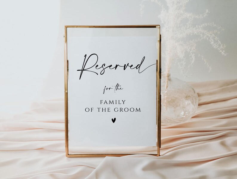May include: A gold-framed sign with the text "Reserved for the Family of the Groom" in black lettering. A small heart symbol is below the text.