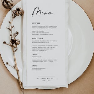 K&ouml;nnte beinhalten: Eine Hochzeitskarte auf einer wei&szlig;en Serviette, pr&auml;sentiert auf einem wei&szlig;en Teller. Die Speisekarte zeigt den handgeschriebenen Titel "Menu" und eine Liste von Vorspeisen, Hauptgerichten, Dessert und Getr&auml;nken. Die Speisekarte ist mit einer getrockneten Pflanze verziert.