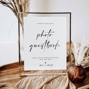 K&ouml;nnte beinhalten: Ein gerahmtes Schild mit den Worten "photo guestbook" in eleganter Schrift. Das Schild enth&auml;lt auch den Text "Kindly sign our" und "Leave your photo & wishes for the new mr and mrs". Der Rahmen ist goldfarben, und der Hintergrund enth&auml;lt dekorative Elemente.