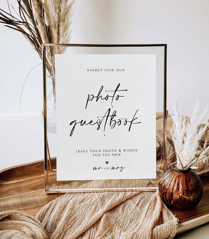 K&ouml;nnte beinhalten: Ein gerahmtes Schild mit den Worten "photo guestbook" in eleganter Schrift. Das Schild enth&auml;lt auch den Text "Kindly sign our" und "Leave your photo & wishes for the new mr and mrs". Der Rahmen ist goldfarben, und der Hintergrund enth&auml;lt dekorative Elemente.
