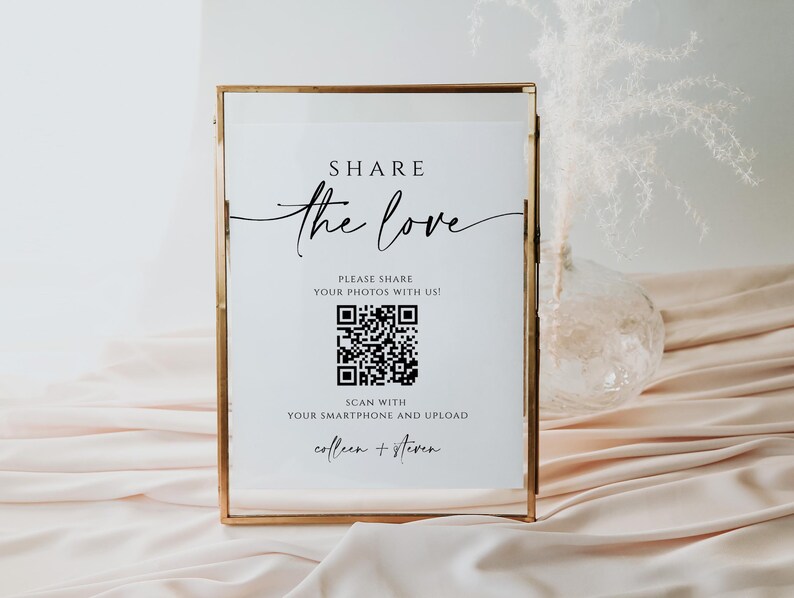 May include: A white sign in a gold frame with the text "SHARE the love" and a QR code. The text below the QR code says "PLEASE SHARE YOUR PHOTOS WITH US!" and "SCAN WITH YOUR SMARTPHONE AND UPLOAD colleen + steven".
