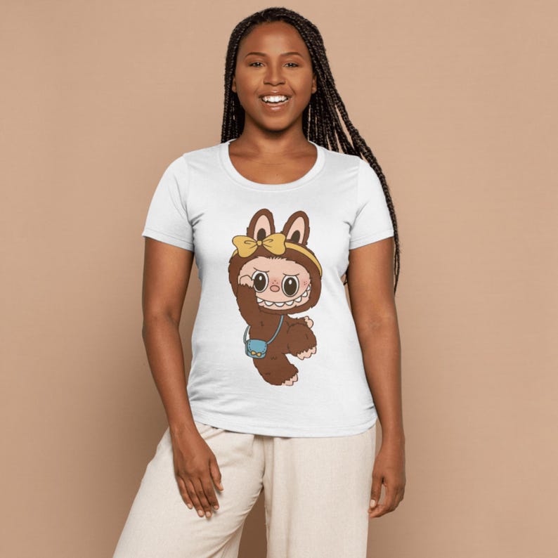 May include: White t-shirt featuring a cartoon character in a brown furry costume with a yellow bow and a small blue purse. The character has large eyes and a wide smile. The shirt is a crew neck style.