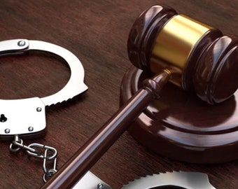 May include: A wooden gavel with a gold top rests on a wooden block. A pair of silver handcuffs are lying on a wooden surface.