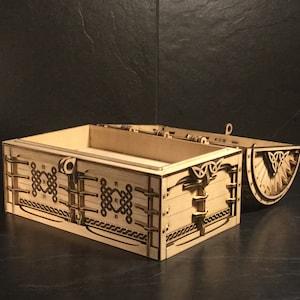 May include: A wooden box with a hinged lid, decorated with intricate Celtic knotwork designs. The box is open, revealing the empty interior.
