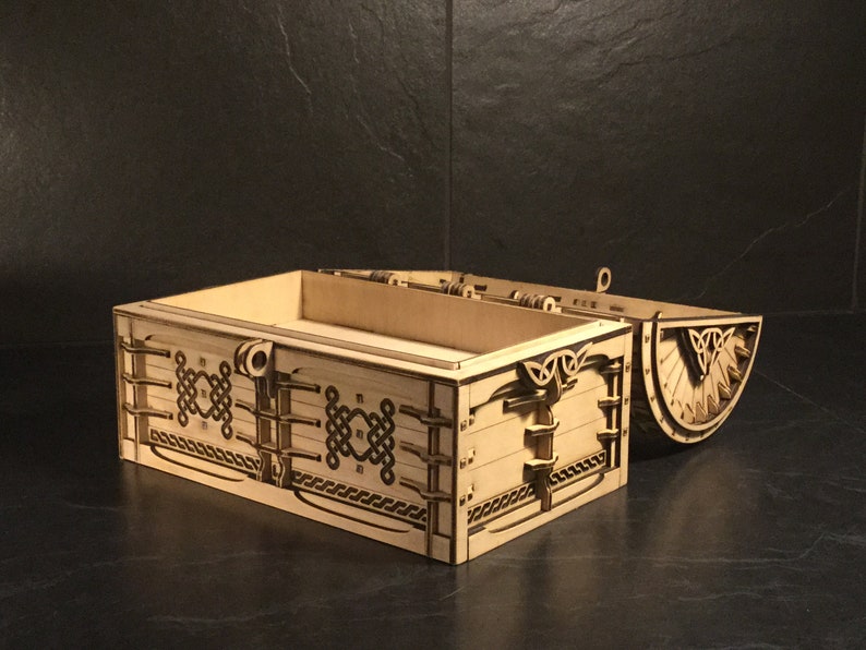 May include: A wooden box with a hinged lid, decorated with intricate Celtic knotwork designs. The box is open, revealing the empty interior.