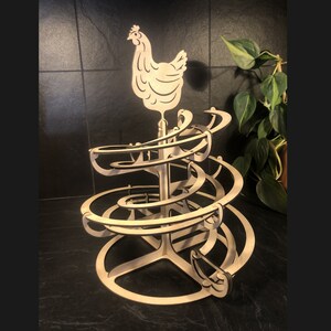 Op de afbeelding: Een houten speelgoed met een kip bovenop en een spiraalvormige baan voor knikkers. De baan bestaat uit meerdere niveaus en de kip is wit.