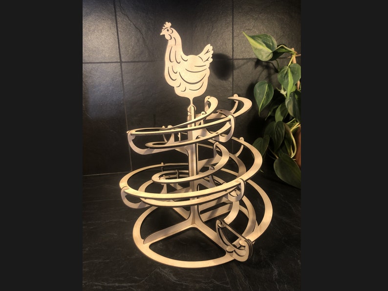 Op de afbeelding: Een houten speelgoed met een kip bovenop en een spiraalvormige baan voor knikkers. De baan bestaat uit meerdere niveaus en de kip is wit.