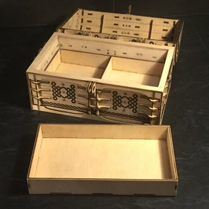 May include: A wooden box with a hinged lid and a removable tray. The box has a decorative design of Celtic knots on the front and sides. The box is open and the tray is removed.