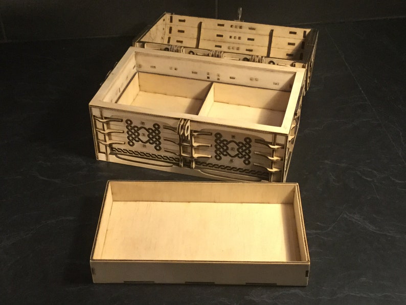 May include: A wooden box with a hinged lid and a removable tray. The box has a decorative design of Celtic knots on the front and sides. The box is open and the tray is removed.