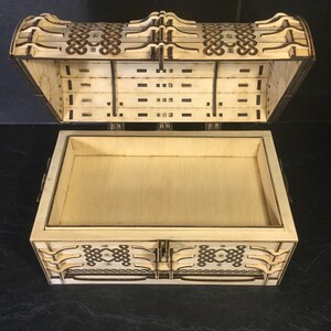 May include: A wooden box with a hinged lid, featuring an intricate Celtic knot design carved into the wood. The box is open, revealing an empty interior.