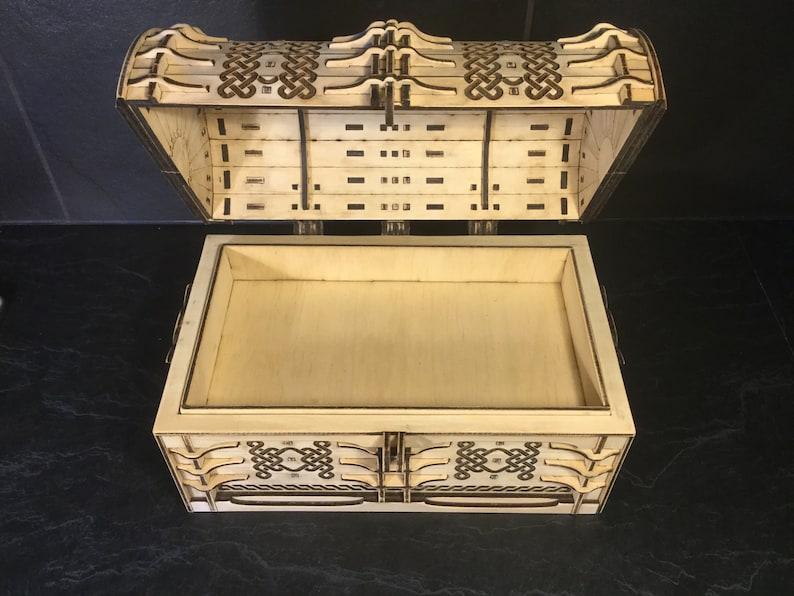 May include: A wooden box with a hinged lid, featuring an intricate Celtic knot design carved into the wood. The box is open, revealing an empty interior.