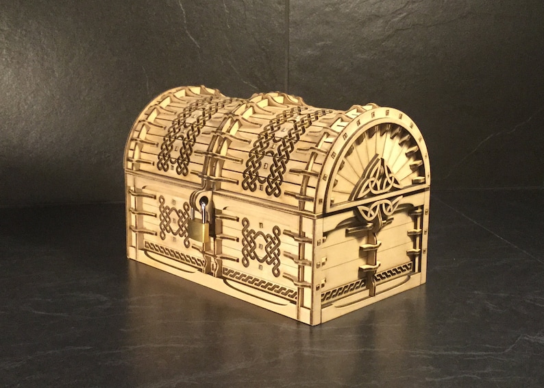 May include: A wooden treasure chest with a Celtic knot design and a lock. The chest is closed and has a light brown finish.