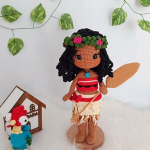 Op de afbeelding: Een gehaakte pop van Moana uit de Disney-film Vaiana. De pop draagt een rood-wit topje, een bruine rok en een bloemenkroon. Ze houdt een bruin houten peddel vast.