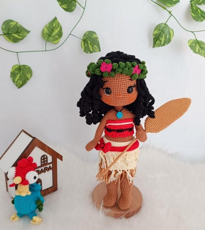 Op de afbeelding: Een gehaakte pop van Moana uit de Disney-film Vaiana. De pop draagt een rood-wit topje, een bruine rok en een bloemenkroon. Ze houdt een bruin houten peddel vast.