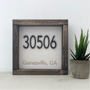 May include: A wooden sign with a white background and black lettering. The sign reads "30506 Gainesville, GA".