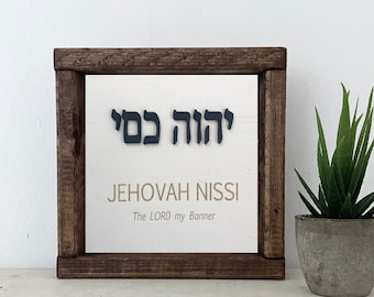May include: A wooden framed sign with the Hebrew words "Jehovah Nissi" and the English translation "The LORD my Banner".