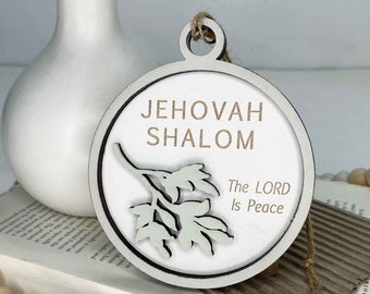 May include: White wooden ornament with the text "Jehovah Shalom" and "The Lord is Peace" in a brown font. The ornament features a green leafy branch design.