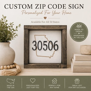 May include: A square wooden sign with a dark brown frame and a white center panel. The center features a tan outline of the state of Georgia with the black numbers 30506 centered over it. Text at the top reads CUSTOM ZIP CODE SIGN.