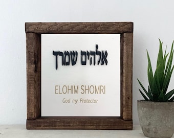 May include: A wooden framed sign with the Hebrew text "Elohim Shomri" and the English translation "God my Protector".