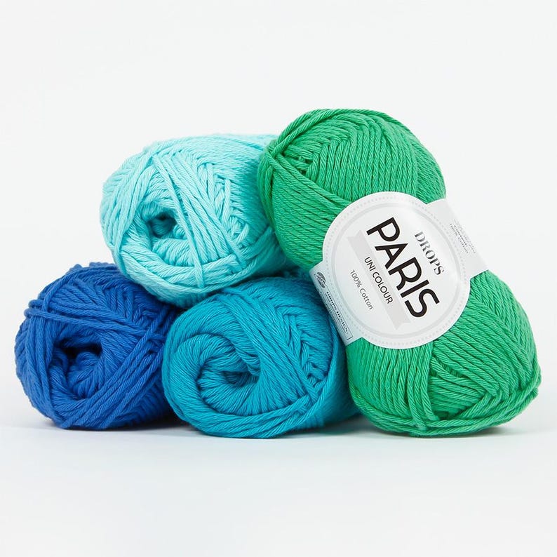 May include: A collection of colorful yarn balls in shades of blue and green. One ball has a label that reads "DROPS PARIS UNI COLOUR 100% Cotton". The yarn is tightly wound, suggesting it's suitable for knitting or crochet projects.