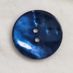 Può includere: Un bottone grande e rotondo con una finitura lucida e iridescente in tonalità blu intenso e sfumature di viola. Il bottone ha due piccoli fori per cucire e una superficie lucida. Adatto per abbigliamento e progetti di artigianato.