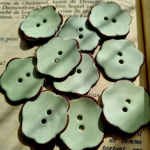 May include: Nine green ceramic buttons with a brown rim. The buttons are shaped like a flower with five petals.