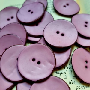 Könnte beinhalten: Nahaufnahme eines Stapels violetter Knöpfe mit jeweils zwei Löchern. Die Knöpfe sind rund und haben einen leicht erhöhten Rand.