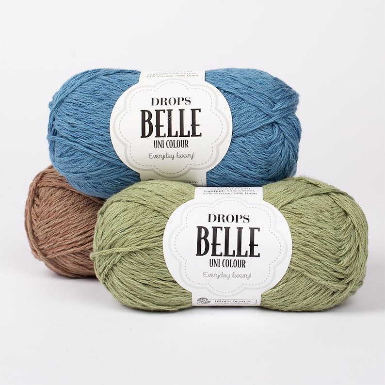 以下が含まれることがあります： 青、茶色、緑色のDrops Belle Uni Colourの毛糸が3玉。各玉にはブランド名と製品詳細が記載された白いラベルが付いています。この毛糸は、レーヨン、リネン、綿の混紡です。