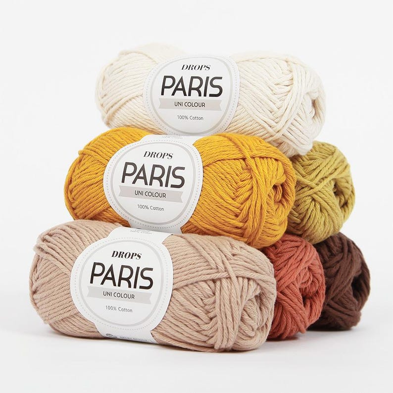 May include: A stack of Drops Paris Uni Colour yarn balls in various colors, including cream, mustard yellow, light brown, and rust. Each ball has a label with the brand name and fiber content.
