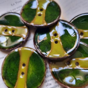 Op de afbeelding: Zes groene en gele keramische knopen met een glanzende afwerking. De knopen hebben een tweekleurig ontwerp met een gele kern en groene randen.